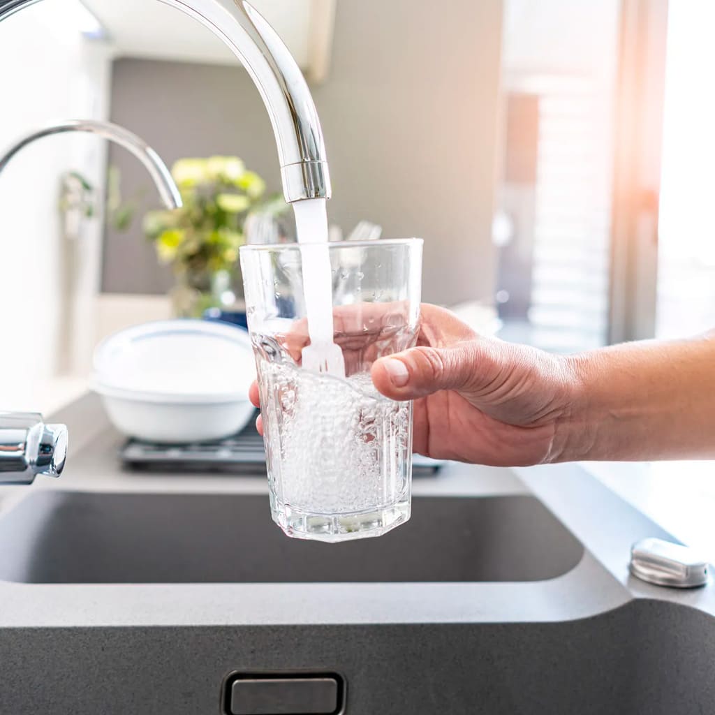 mano de un hombre llenando un vaso de agua en un grifo